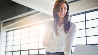 woman looking at her computer while drinking coffee in office